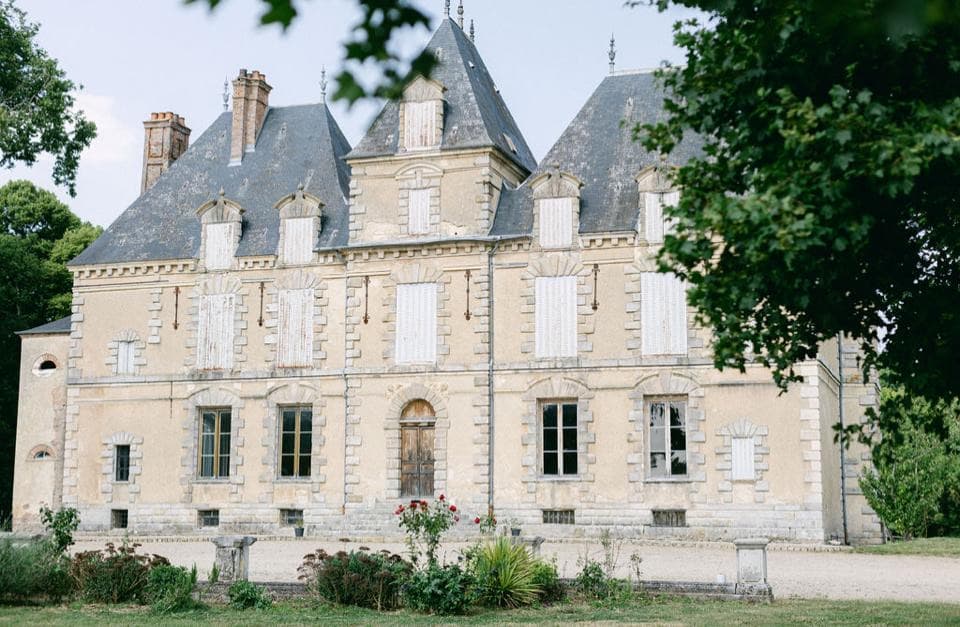 Façade du château de Motteux encadrée par le feuillage des arbres du parc en été
