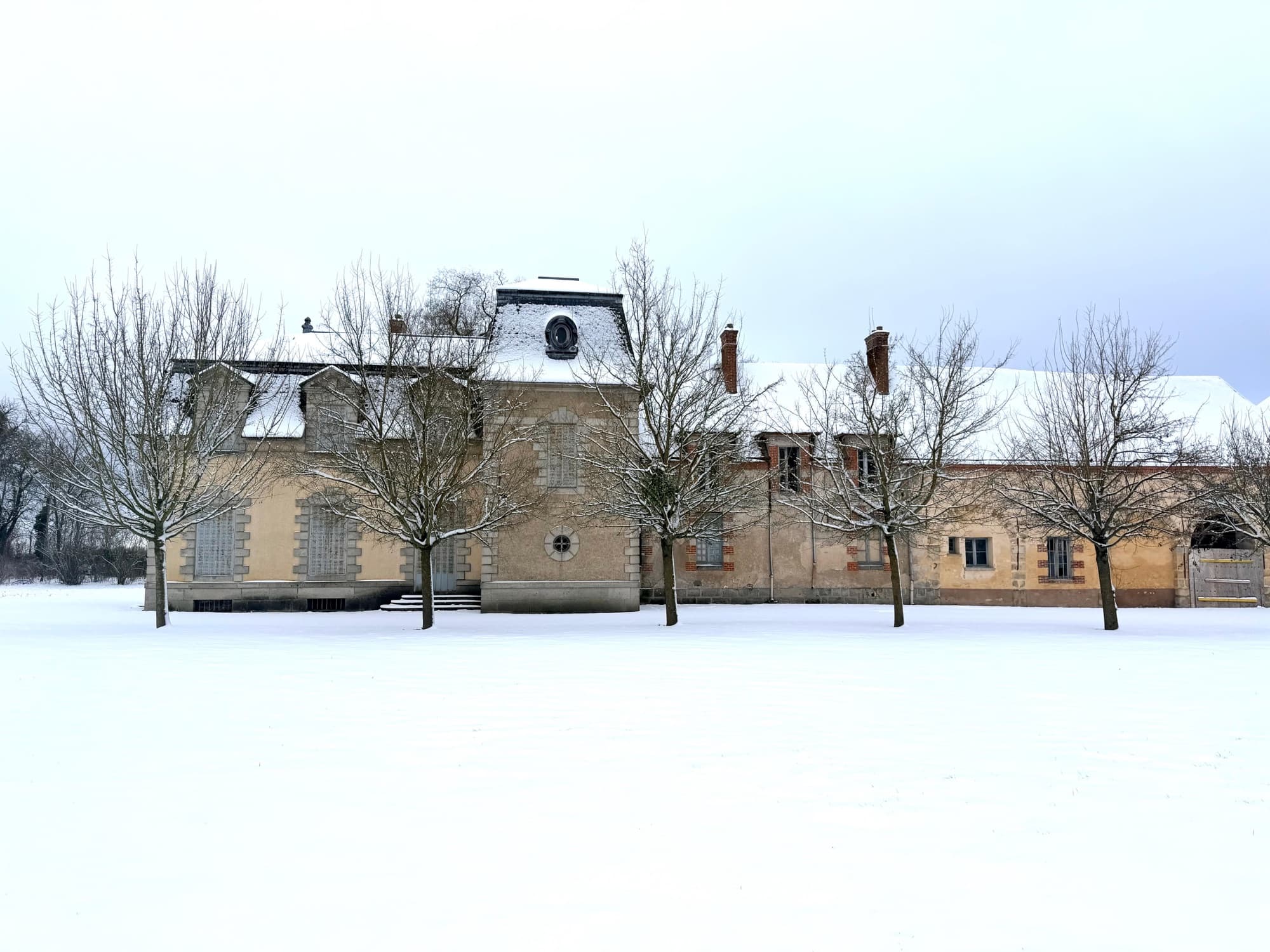 Dépendances du château de Motteux derrière les arbres du parc enneigé