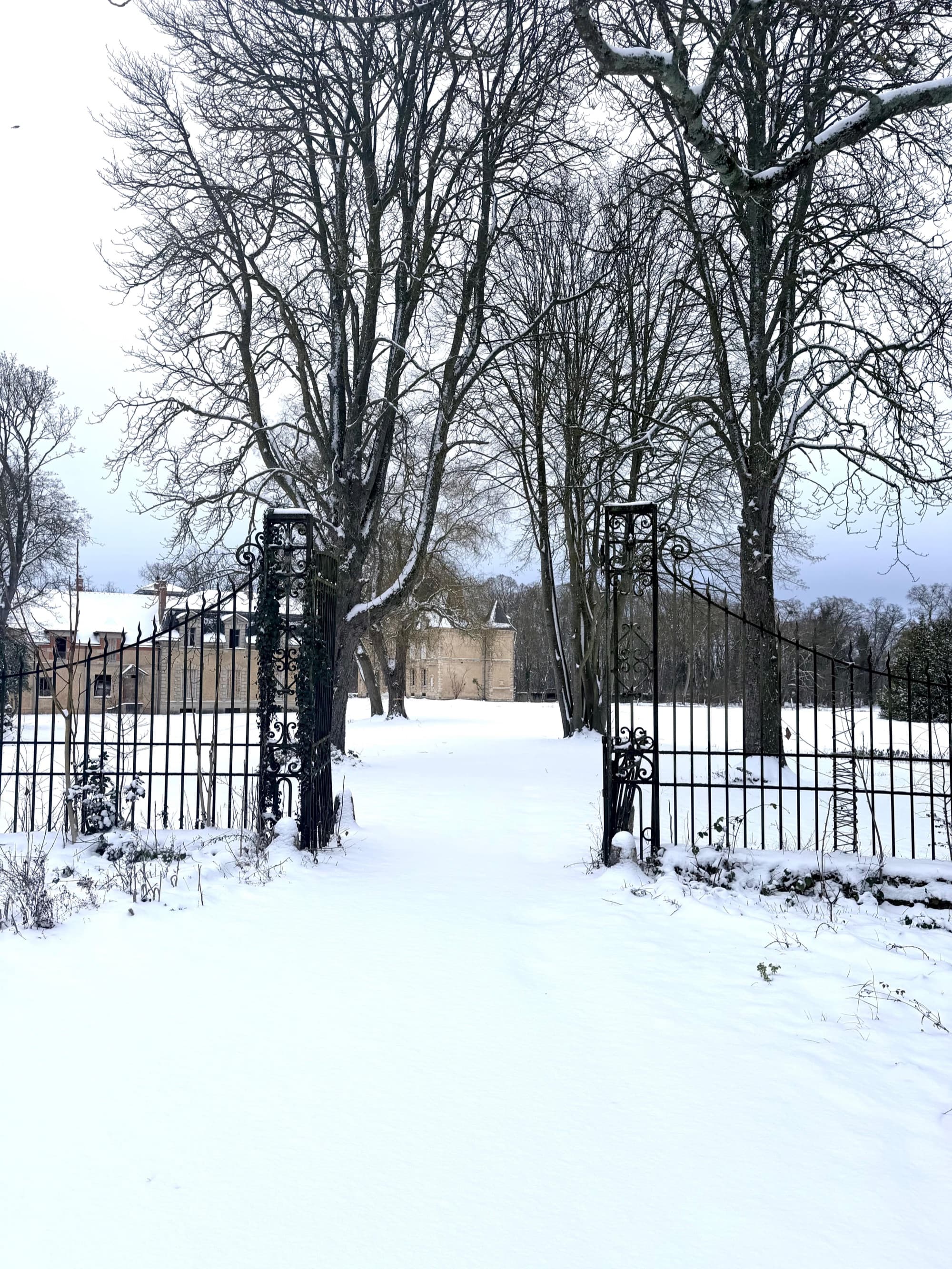 Allée enneigée du parc menant au château de Motteux entre les grilles en fer forgé