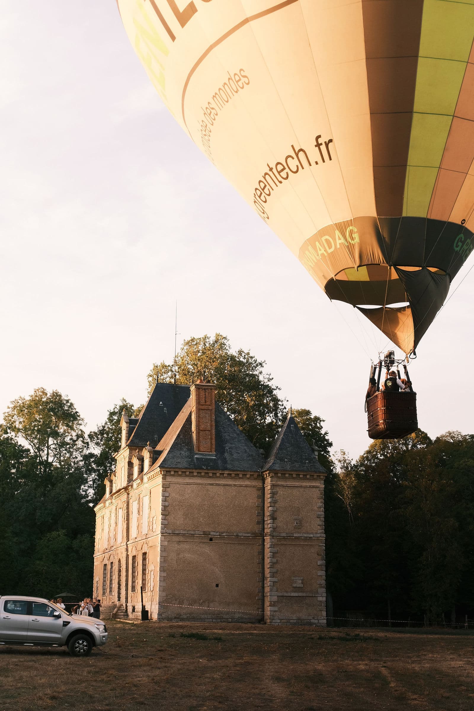 Montgolfière passant au ras des toits du château de Motteux, nacelle et passagers au-dessus du domaine