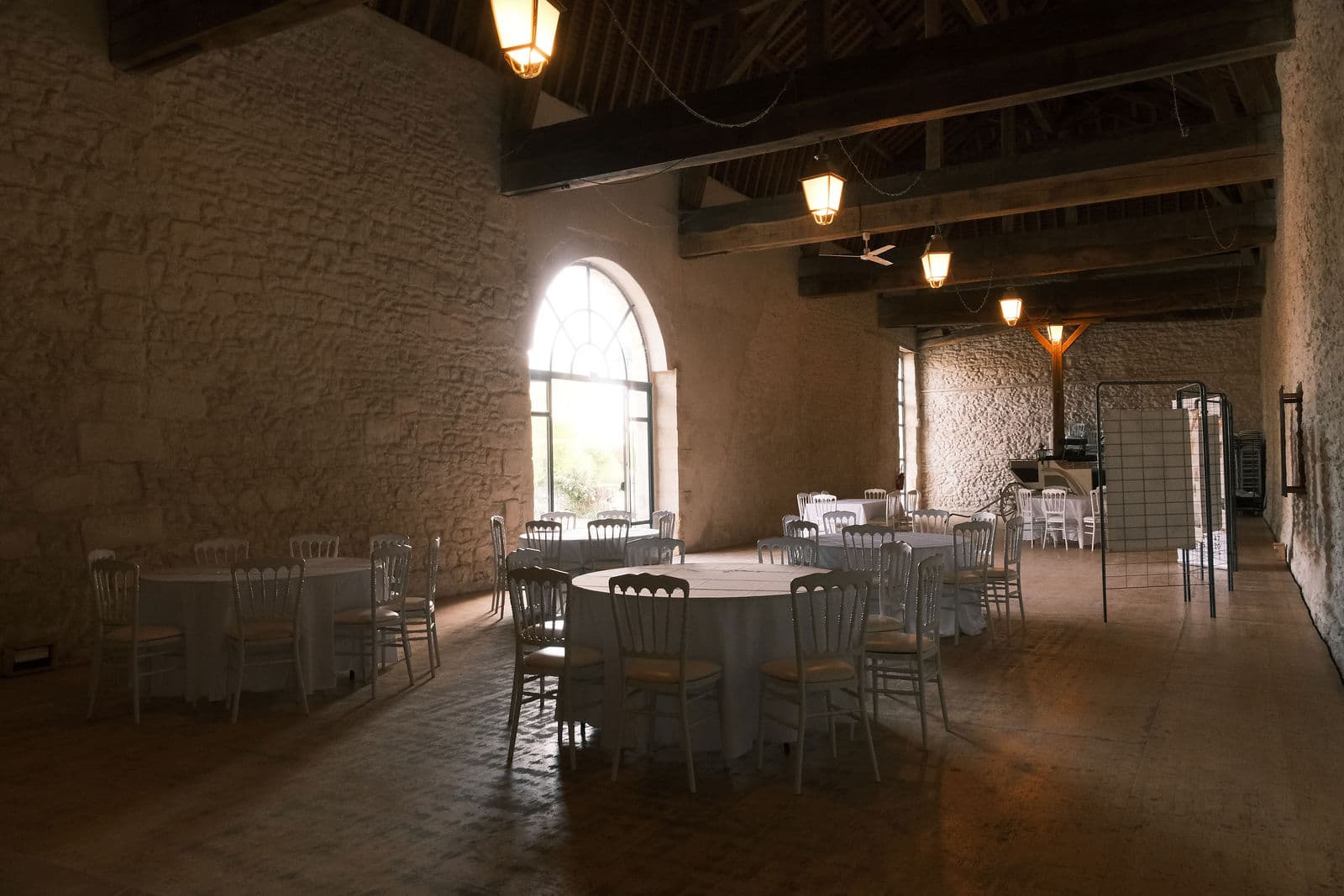 Grange Henri II du château de Motteux dressée pour un dîner, tables rondes et lanternes sous la charpente