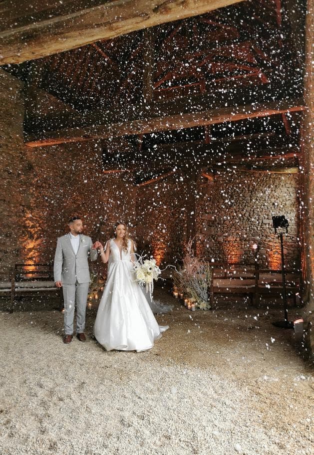 Entrée des mariés sous une pluie de confettis dans la grange en pierre du château de Motteux