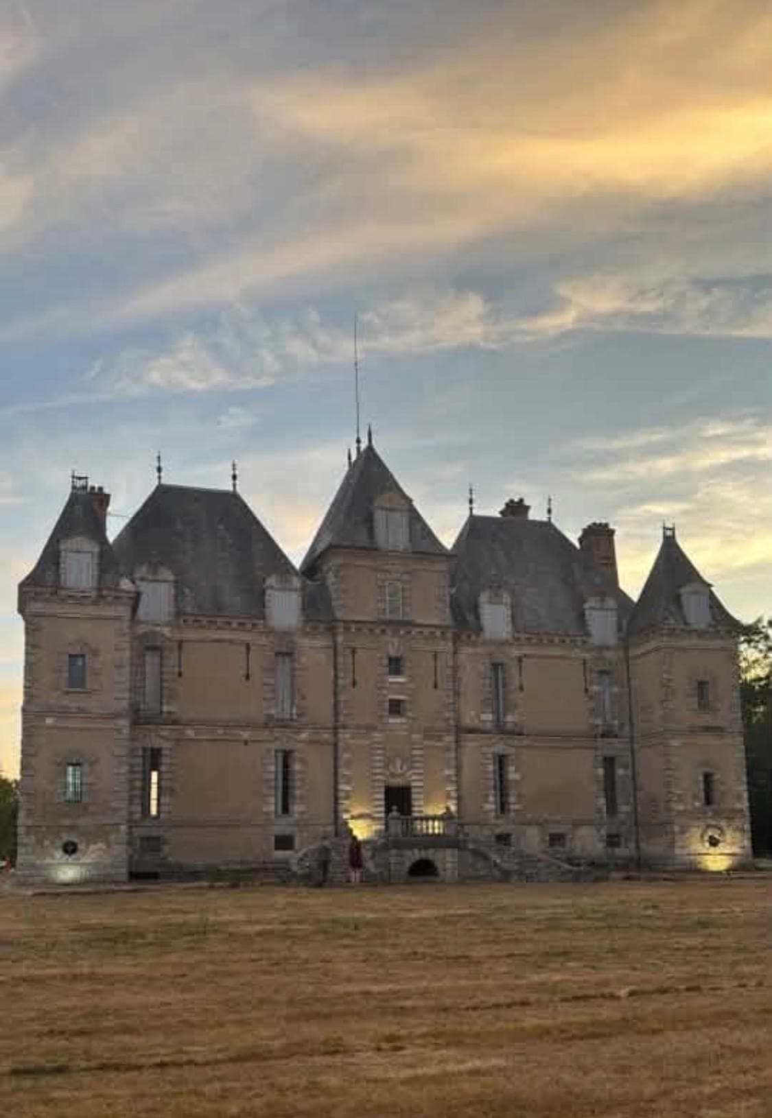 Façade du château de Motteux illuminée au coucher du soleil sous un ciel doré