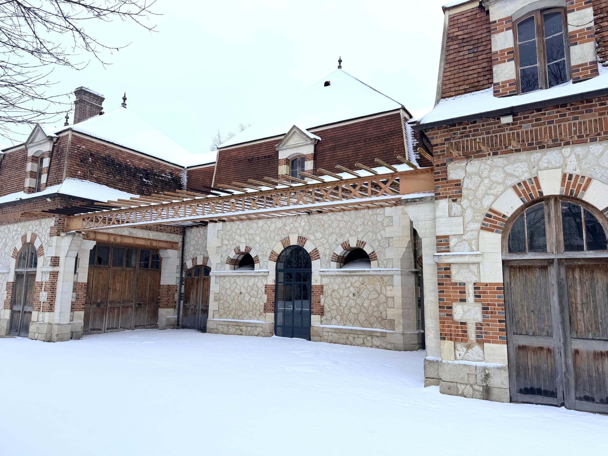 Communs en pierre et brique du château de Motteux sous la neige, pergola métallique et portes anciennes