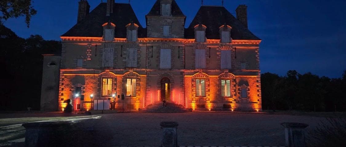 Château de Motteux illuminé d’orange à la tombée de la nuit lors d’une soirée dans le parc