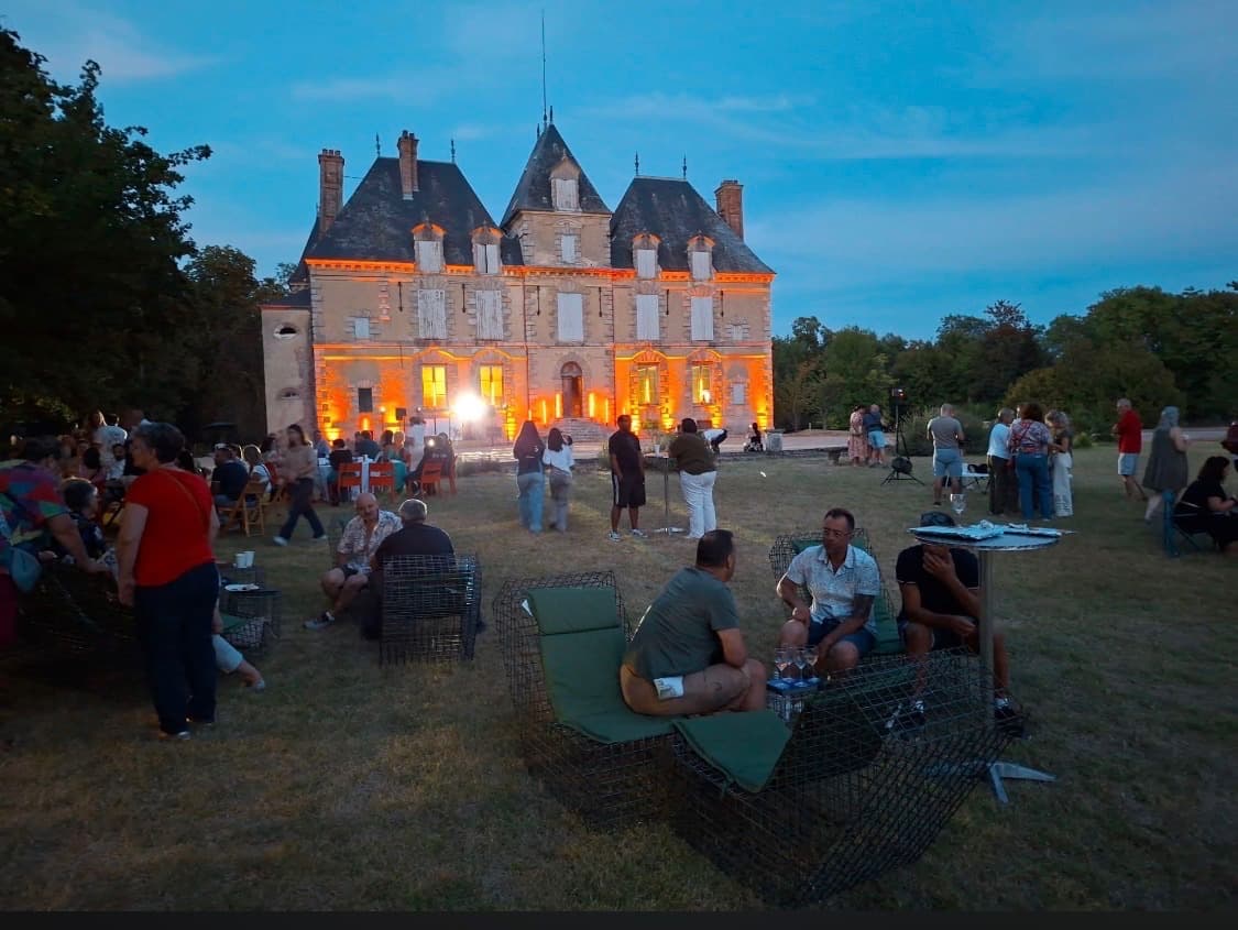 Guinguette au château de Motteux à la tombée de la nuit, façade illuminée d’orange et visiteurs sur la pelouse