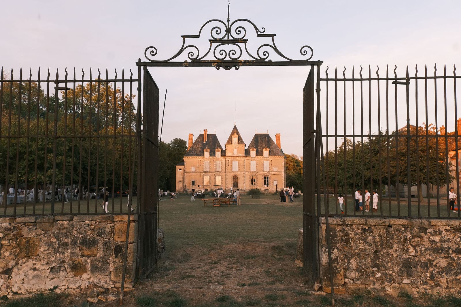 Grille d’honneur ouverte sur le château de Motteux un soir de soirée blanche, convives en blanc sur la pelouse