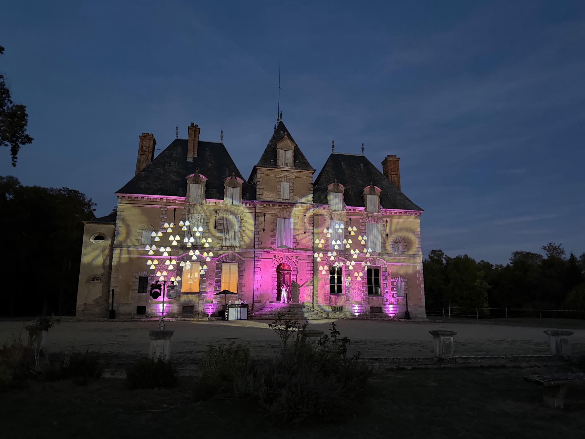 Façade du château de Motteux illuminée de rose et d’or à la nuit tombée, motifs projetés sur la pierre