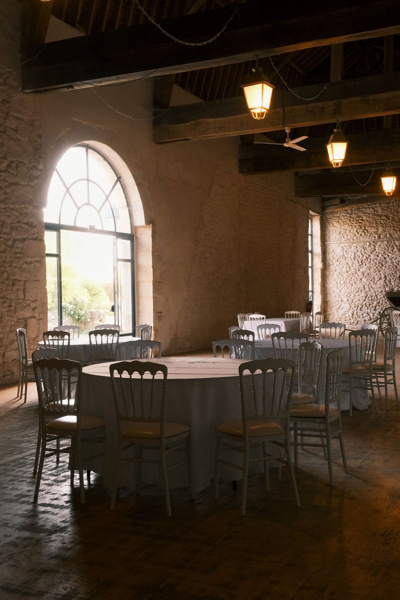 Grande fenêtre cintrée de la grange Henri II du château de Motteux, tables rondes dressées sur le sol ancien